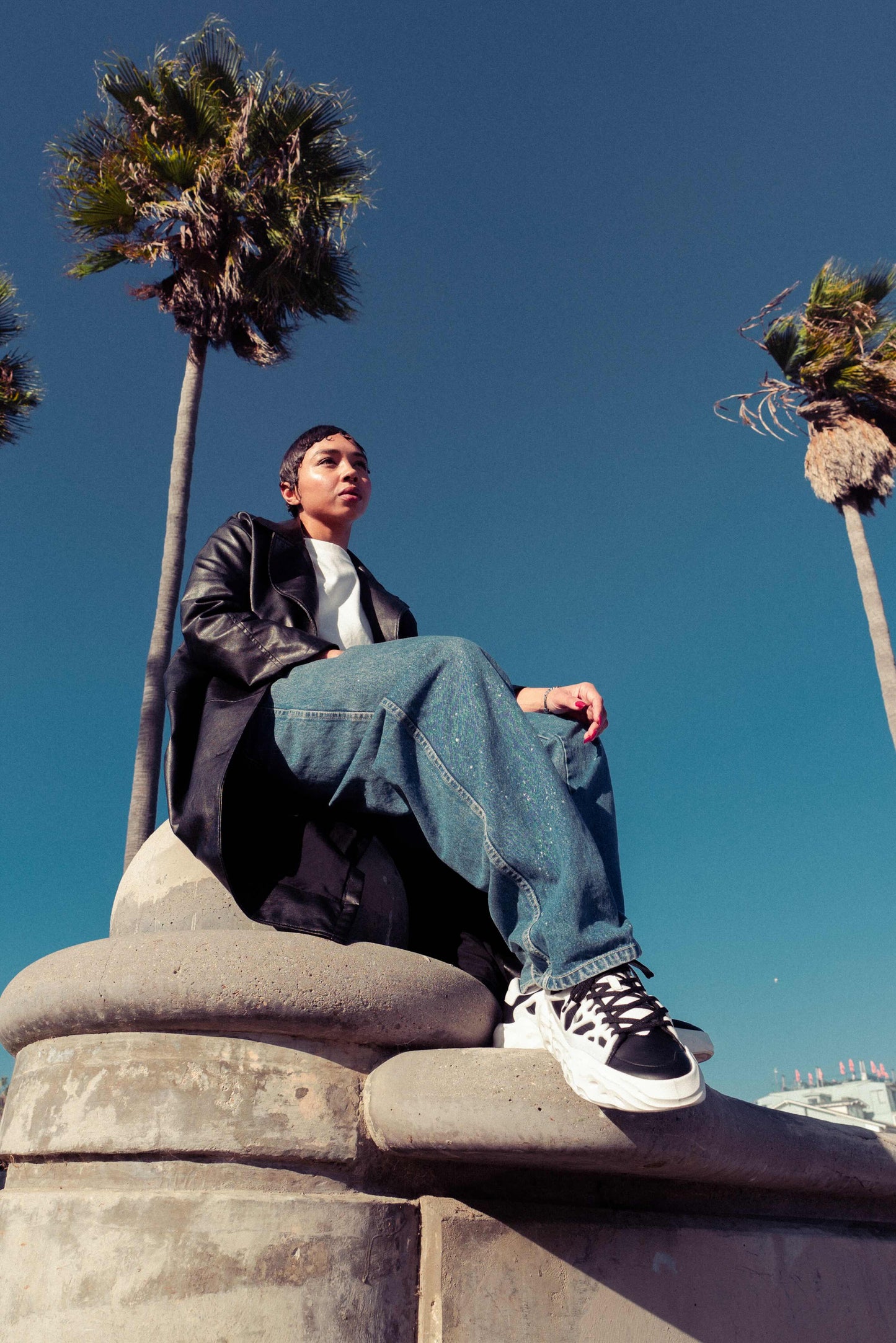 Flowers For Society Sneaker Radicle Orca black white sideview worn by model sitting on concrete sculpture