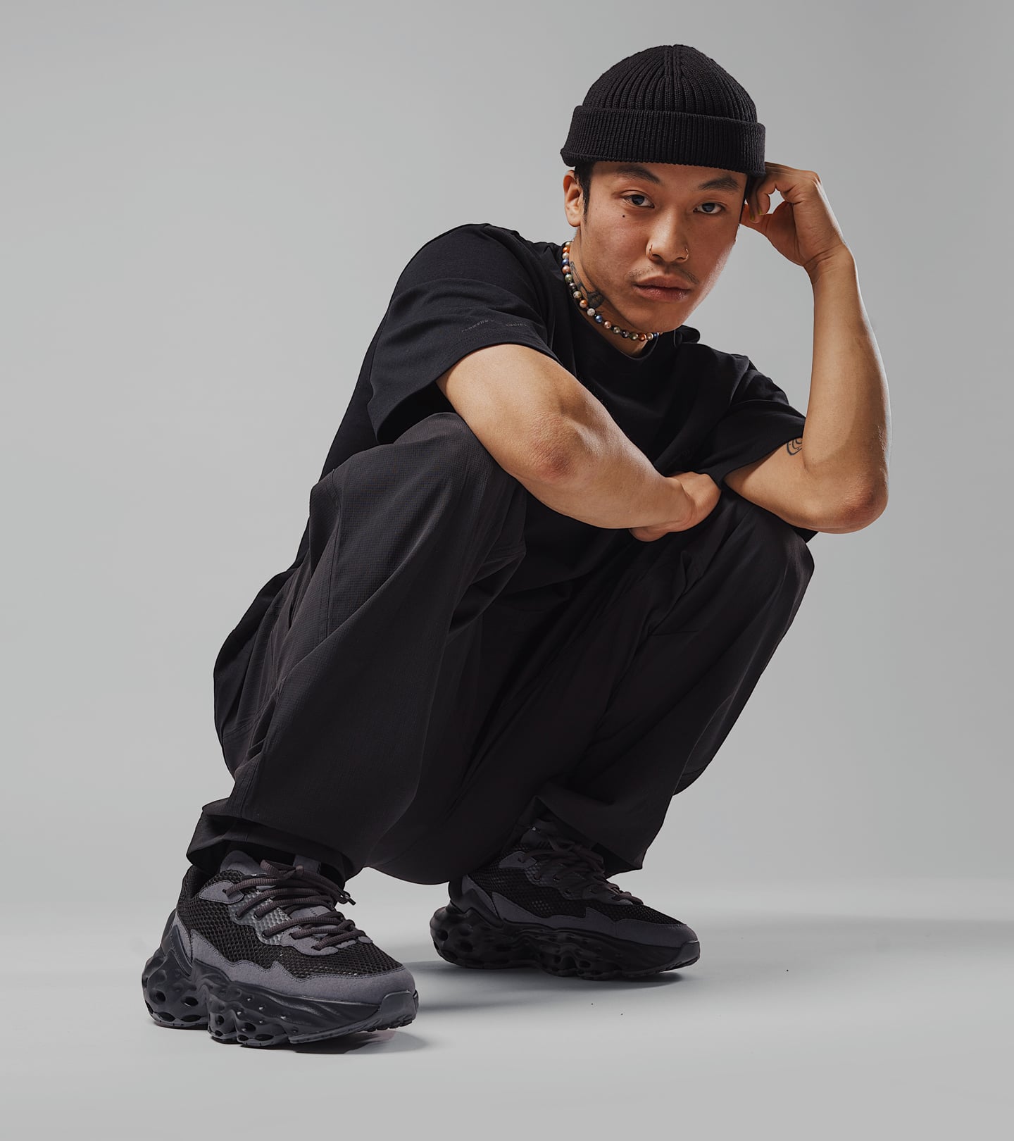 Campaign photo of a male model sitting in a squat position, wearing the Seed.One Black Mud colorway and Black Mud apparel