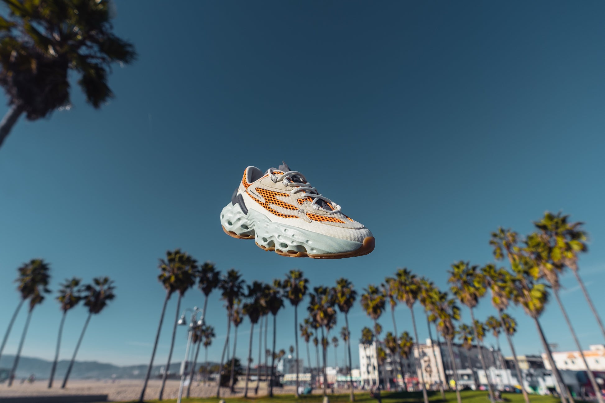Flowers for Society Sneaker Seed.One Detox orange sideview flying in the air at a beach