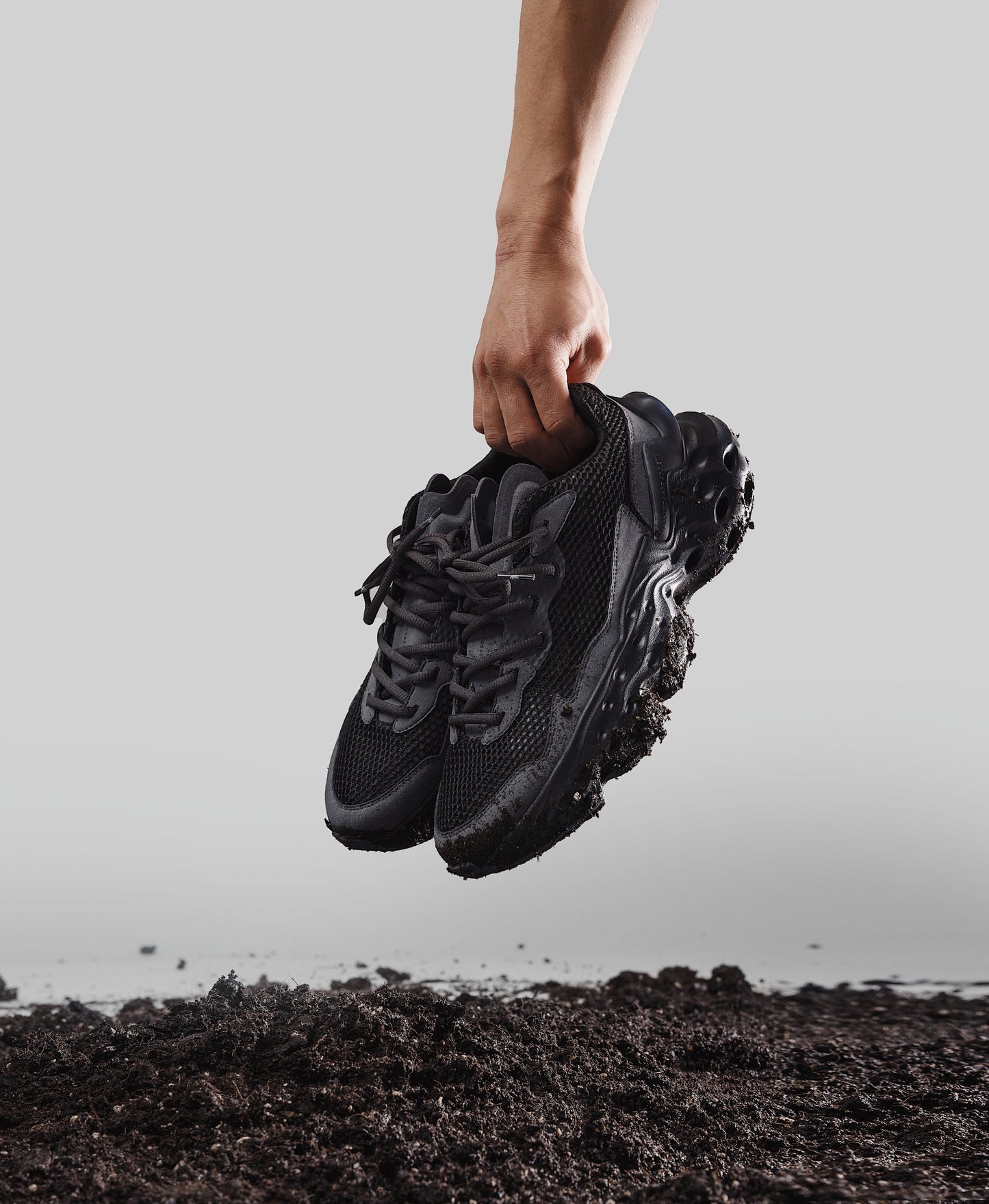 Flowers for Society Sneaker Seed.One Black Mud black sideview held by a hand above a pile of earth