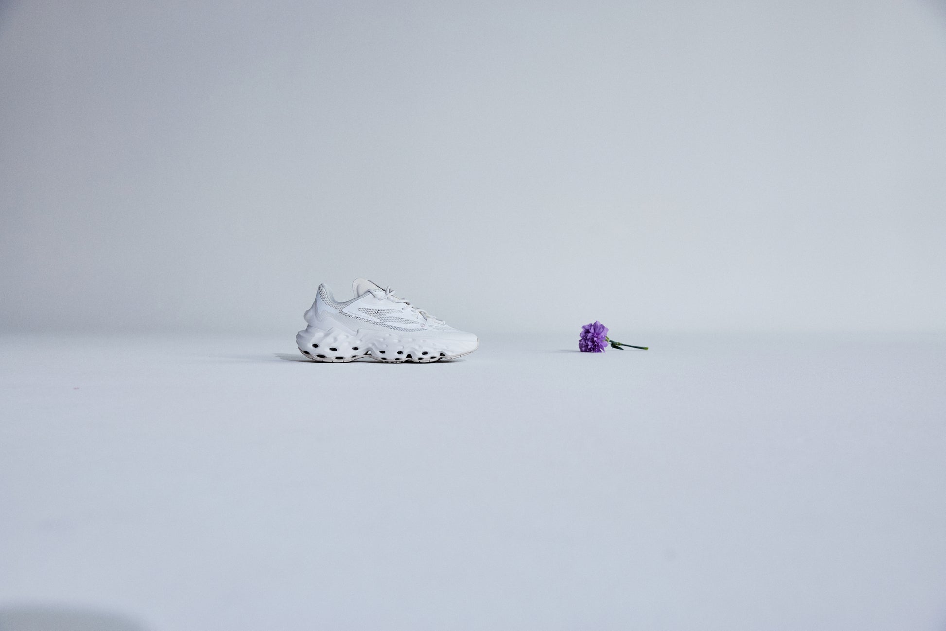 The shoe Seed.One in the colorway White Lily from the lateral side, with a purple flower placed to it's right.